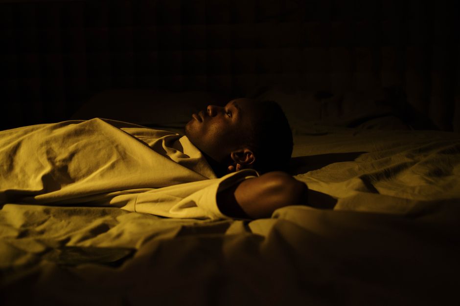 A man asleep in bed in a dimly lit, warm-toned room