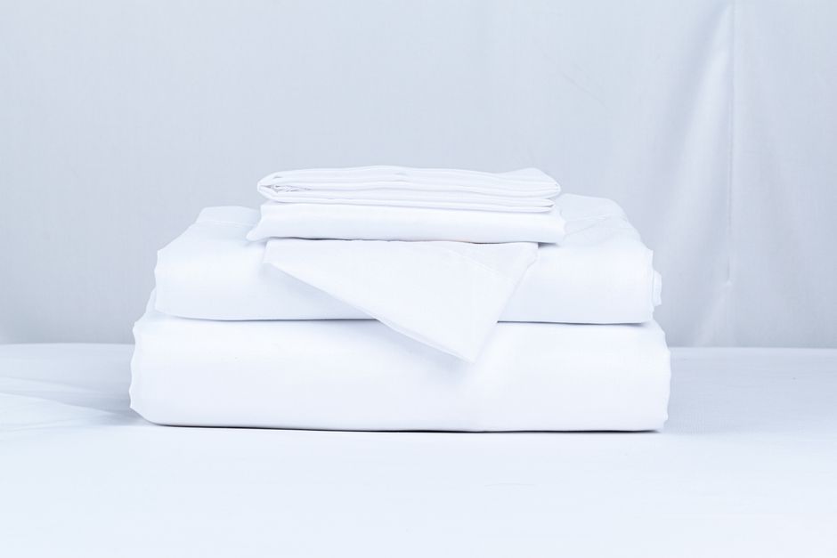 A stack of folded white bed linen on a plain surface